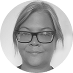 Black and white portrait of a person with light-coloured hair pulled back, wearing large, dark-framed glasses, and a slight smile, facing the camera against a plain background.